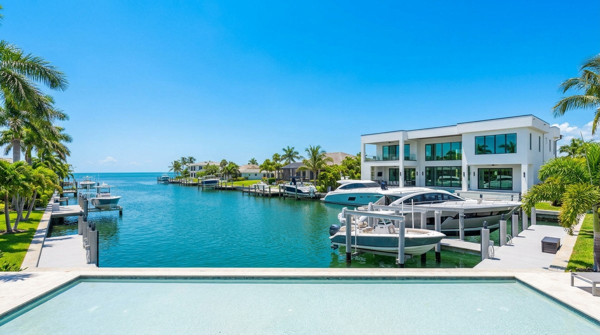A modern Cape Coral waterfront luxury home with a pool, multiple boats docked, and palm trees under a blue sky.